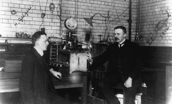 Ernest Rutherford in the lab: Ernest Rutherford sitting in his lab (right) with his assistant, Hans Geiger. Circa 1913. Credit: Reference number PAColl-0091-1-011, Sir Ernest Marsden Collection, Alexander Turnbull Library, Wellington, New Zealand.